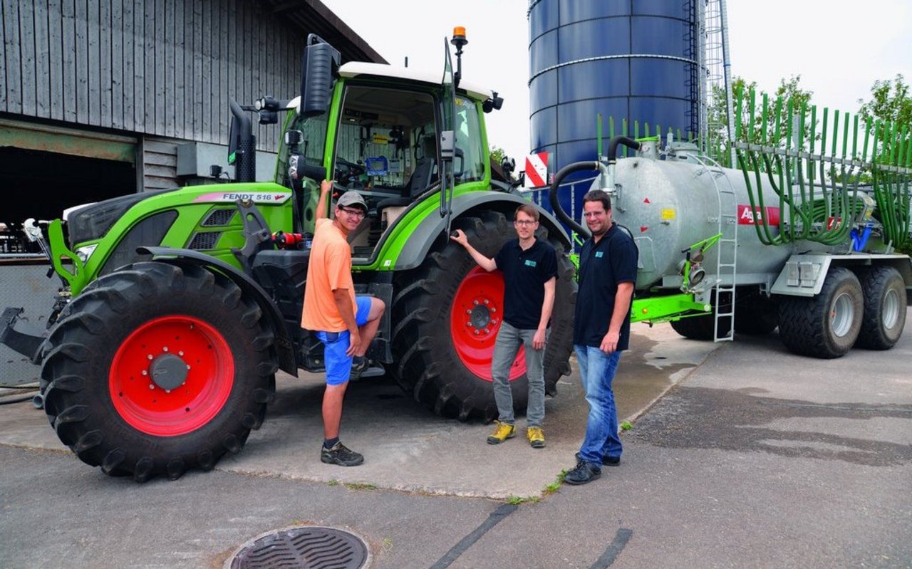 Flavio Näf (links), Florian Abt (Mitte) und Marco Landis (rechts) von der Swiss Future Farm stehen vor dem Traktor, an dem ein Güllefass angehängt ist.