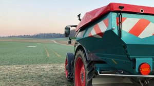 ein Traktor mit angehängtem Düngerstreuer steht am Rand eines Weizenfelds.